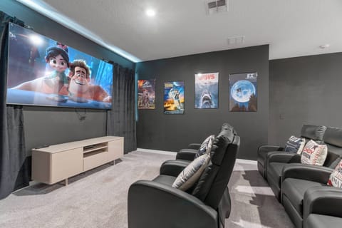 Enjoy a cinematic experience with plush reclining chairs and a large wall-mounted TV, perfect for movie nights. The cozy ambiance, rich dark walls, and colorful film posters create a nostalgic and engaging atmosphere for all.