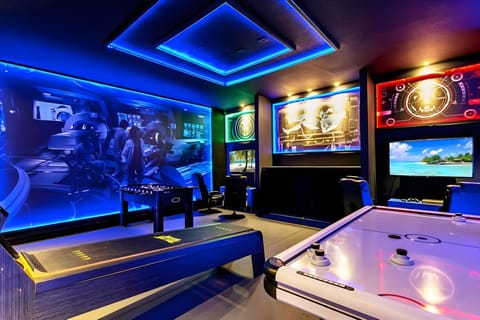 Discover a lively entertainment oasis with striking blue lighting and modern decor. Engage in friendly competition at the air hockey table, all while enjoying captivating wall art and multiple screens for an immersive experience.
