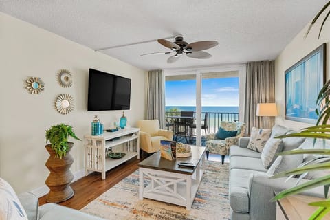 Your coastal living room features plush seating, ocean views through floor-to-ceiling windows, and a perfect breeze from the ceiling fan.