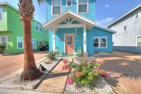Charming coastal cottage with bright blue siding and welcoming entrance, nestled among colorful beach houses.