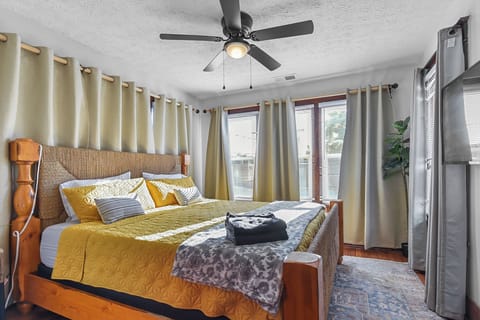 Drift off to sleep in this cozy bedroom with warm yellow linens, a ceiling fan keeping you cool, and natural light filtering through your windows.