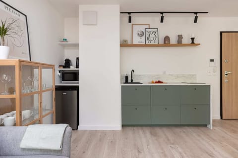 A modern kitchen with a simple design, featuring light green cabinetry and open shelving, giving it a clean and uncluttered appearance.