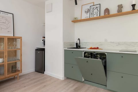 A modern kitchen with a simple design, featuring light green cabinetry and open shelving, giving it a clean and uncluttered appearance.