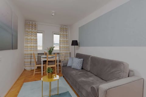 Living room with a gray sofa, wooden table, and bright natural light coming through the windows.
