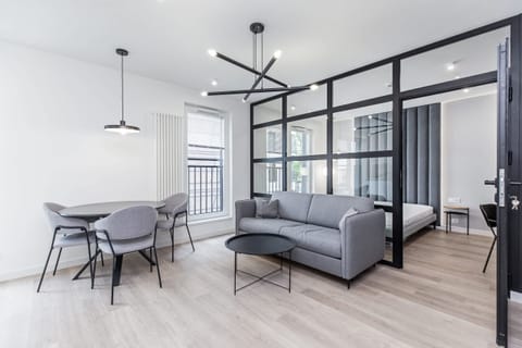 A modern living area featuring floor-to-ceiling black-framed windows, a sleek gray couch, and light wooden floors, blending contemporary design with industrial elements.
