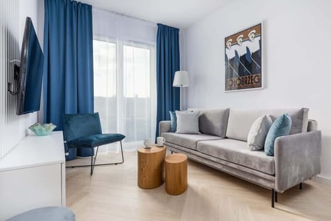 Cozy living room with a gray sofa, wall-mounted TV, and bright natural lighting.
