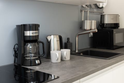 A kitchen counter with a coffee machine, kettle, and white mugs neatly arranged.