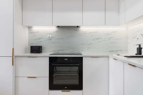 A sleek white kitchen with minimalist cabinetry, a black oven, and a marble backsplash, offering a sophisticated cooking area.

