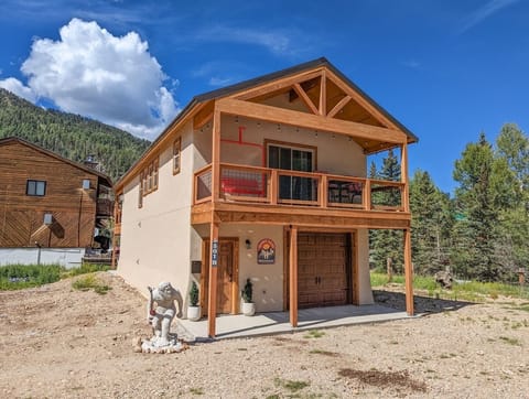 The property sits nestled in a serene mountain setting, surrounded by evergreen trees and framed by stunning natural terrain—a peaceful retreat location.