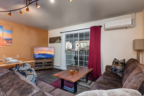 Relax in your comfortable living room featuring a cozy sectional sofa, flat-screen TV, and dining area - perfect for unwinding after your adventures.