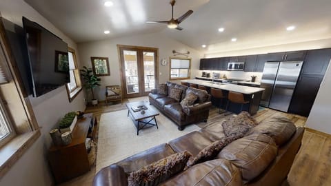 Picture yourself unwinding in this inviting open-concept space—cozy leather sofas face a wall-mounted TV, while sleek modern appliances await your next home-cooked meal in the well-equipped kitchen.