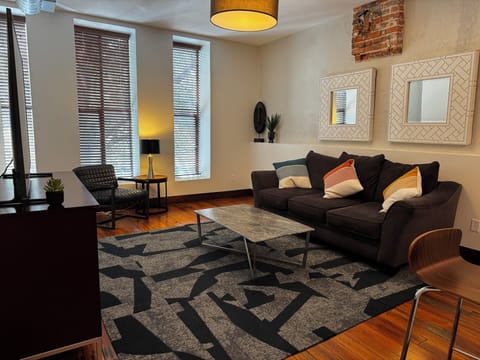Cozy living with plush sofa, bold rug, brick walls, and bright modern charm.