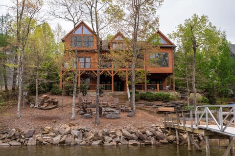 A stunning lakefront home nestled among lush greenery, featuring expansive windows and multiple decks that offer panoramic views of Lake James.