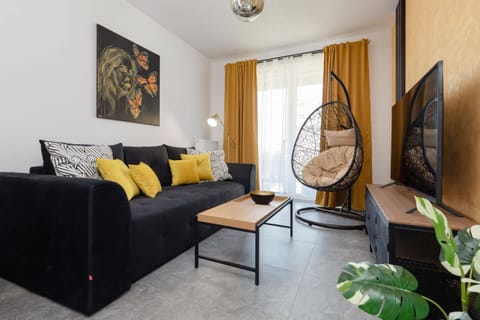 A stylish living room with a gray sofa, vibrant yellow cushions, and a hanging chair. A small coffee table and wall art complete the cozy atmosphere.