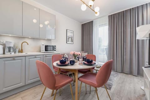 A dining area adjacent to a minimalist kitchen, with a round table and pink chairs.