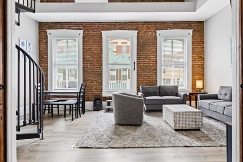 The bright living room pairs tall windows and exposed brick with comfortable seating and the home's spiral staircase.