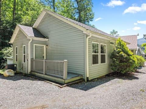 Exterior view of the creekside cottage with gray siding, front windows, and entry deck surrounded by trees in Bryson City, NC. Convenient to downtown Bryson City and Great Smoky Mountain attractions.