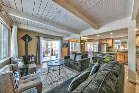 Wood-beamed ceiling tops the living area with gray sofas, patterned rug, and black wood-burning stove by sliding doors.