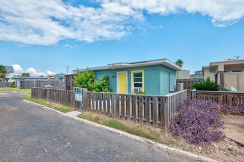 Charming turquoise beach cottage with bright yellow accents sits in a quiet residential neighborhood, offering a peaceful coastal retreat.