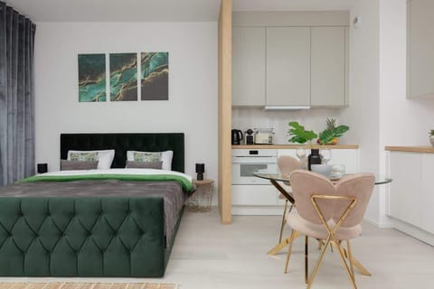 A modern living room with a green velvet sofa, a small wooden dining table, and minimalist decor featuring a neutral color palette.
