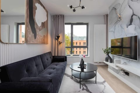A spacious living room with a black sofa, a round coffee table, and a TV mounted on a sleek white cabinet.
