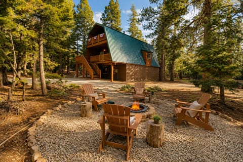 A charming mountain cabin surrounded by towering pines, featuring a cozy fire pit with Adirondack chairs—perfect for gathering under the stars after a day of adventure.