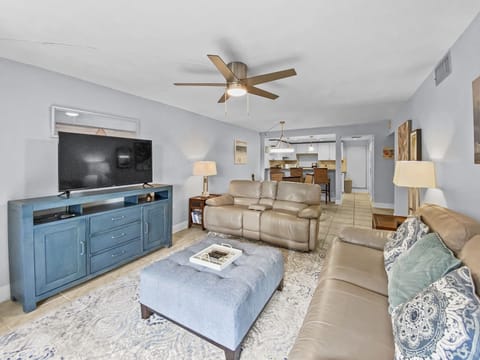 Open living room with TV, blue media console, beige sofas, and ceiling fan