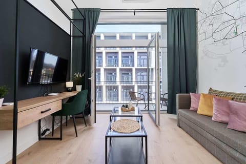 A cozy living room with a sofa, TV, and large windows leading to a balcony with urban views.