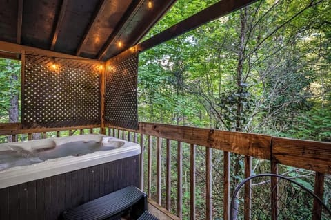 Relax in the private hot tub surrounded by lush forest views, string lights above, and peaceful seclusion on a covered deck.