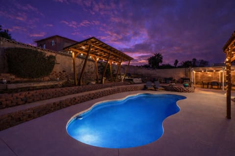 Twilight oasis with lit pool, pergola lounge, and string-lit patio.