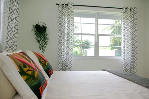 King size bed in airy bedroom with view of front yard with coconut tree.