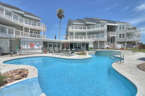 Beachside resort complex featuring a sparkling lagoon-style pool surrounded by multi-story vacation rental buildings with private balconies.
