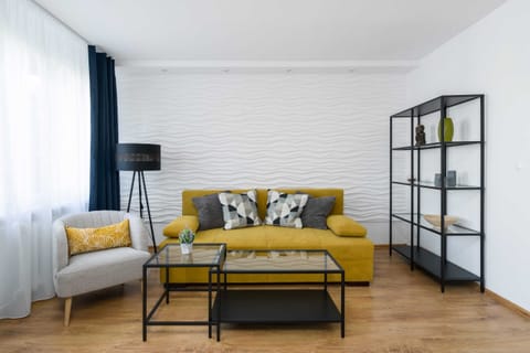 A bright living room featuring a mustard-yellow sofa, decorative pillows, and a modern black coffee table, complemented by large windows.
