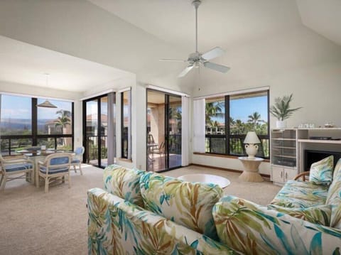 Relax in your bright living room with tropical breezes, vibrant island-style seating, and sweeping views of lush palms and distant mountains through expansive glass doors.