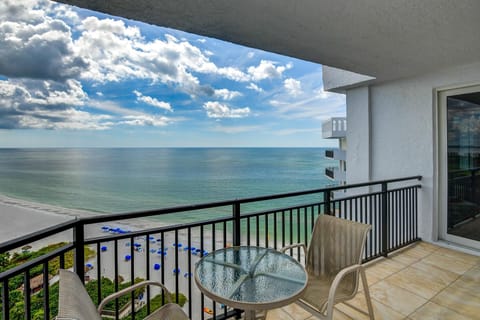 Sliding glass doors open from the living room onto a tiled balcony with a glass-top table and two beige mesh chairs.