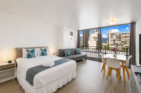 Bright studio with a queen bed, cozy sofa, and private balcony offering city views.