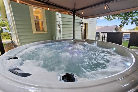 Private backyard features a 7 person hot tub under an all-weather awning, firepit with Adirondack lawn chairs, gas grill and a hammock