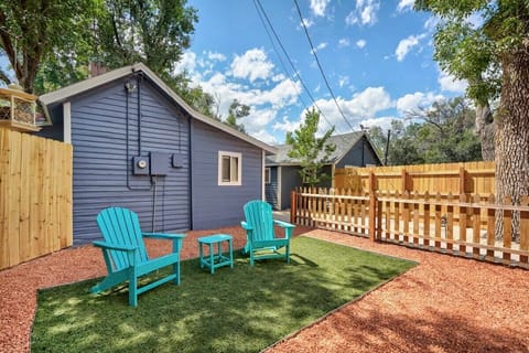 Sunny backyard with two blue Adirondack chairs set on the grass, an easy spot to sit back with a drink, feel the breeze, and enjoy open sky views beside the fenced yard and small house.