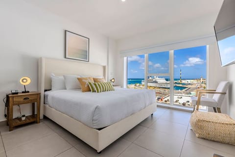 Wake up to stunning ocean views from your plush bed, where soft linens and cheerful accents welcome you. Natural light pours through expansive windows, framing the sparkling sea and marina below.