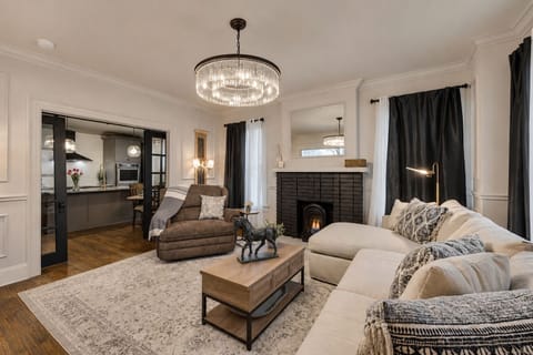 The spacious living room features a comfortable sofa and a cozy gas fireplace, perfect for relaxing. With chic style, a beautiful chandelier, and blackout curtains, the room is bright and inviting, offering a stylish space to unwind.