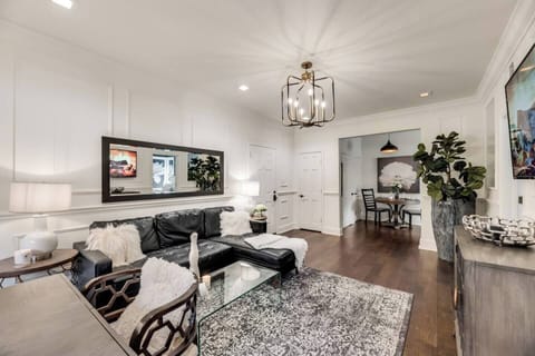 The living room offers a bright and inviting space, with a cozy black sectional couch. In the corner, you'll find a dedicated office workspace, perfect for getting some work done. A beautiful chandelier adds a touch of elegance and warmth to the room.