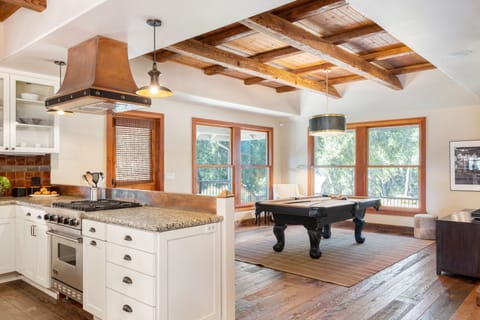 Billiards table near the kitchen is surrounded by windows.