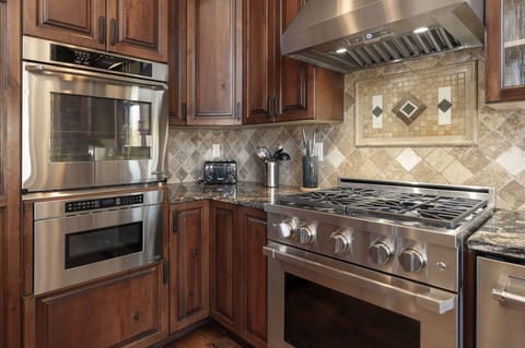 A modern chefs kitchen with stainless steel appliances, including a double oven, gas stove, and range hood
