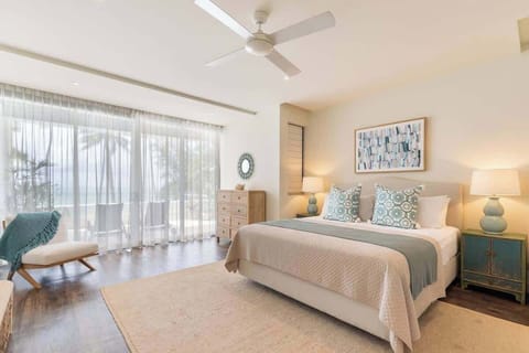 The immaculate primary bedroom boasts a king-size bed and wall-to-wall glass doors showcasing the tropical views from the private balcony