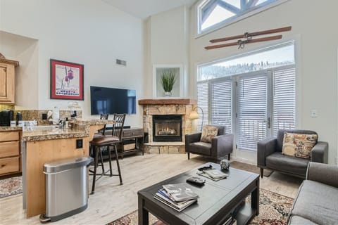 - Cozy living room with stone fireplace and warm mountain decor  
- Large TV and open layout for family relaxation and entertainment  
- Natural light fills the space with views of the scenic outdoors