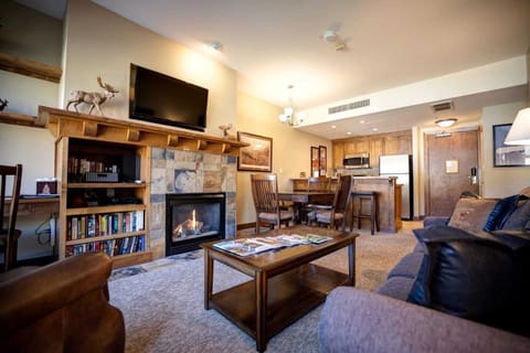Cozy living room featuring a stone fireplace, comfortable seating, and an open layout connecting to the dining area and kitchen.