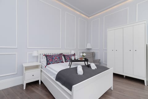 A bright bedroom with a double bed, white furniture, and soft, elegant wall paneling.
