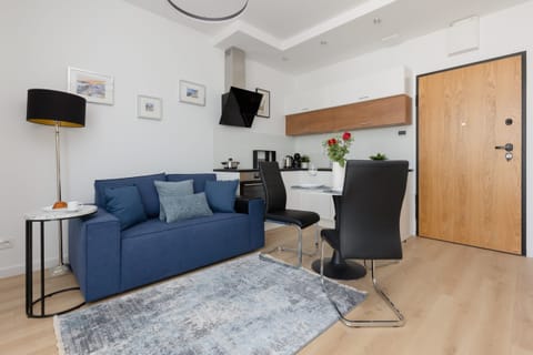 A modern living area with a blue sofa, armchairs, and a wooden door leading into the apartment.

