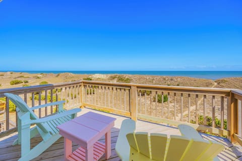 Your private deck overlooks sandy dunes and sparkling turquoise waters, where bright coastal chairs invite you to unwind with endless ocean views and gentle sea breezes.