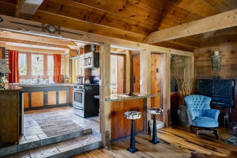 Cozy cabin kitchen with rustic wooden beams, a charming breakfast bar with patterned stools, and a comfy blue armchair perfect for relaxing after a hearty meal.